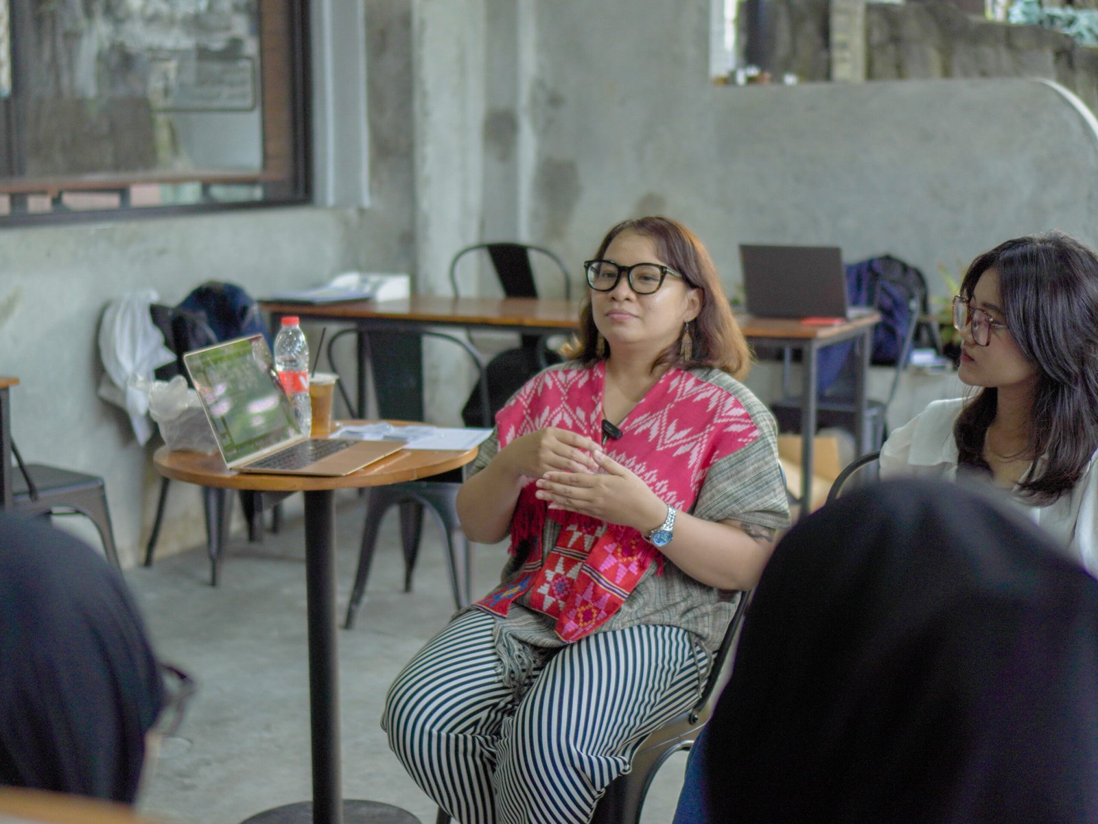 the founder sitting in the chair and in front of some female beneficiaries while speaking to them